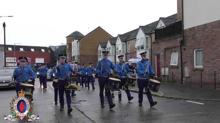 Pride of the East Flute Band marching with drummers in blue shirts