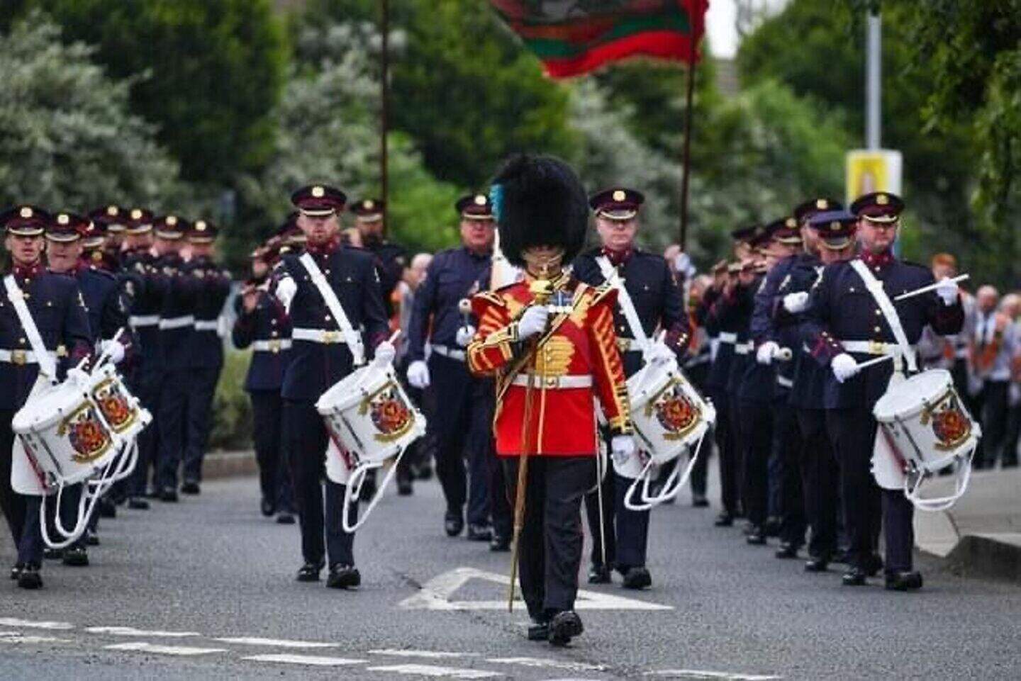 Pride of the Raven Flute Band marching, led by a drum major in a red uniform